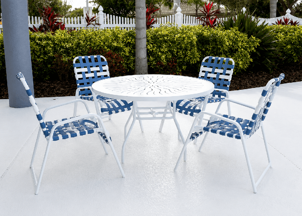 Resort-inspired outdoor dining set with woven vinyl strap chairs and a punch top design round aluminum table on a luxury pool deck.